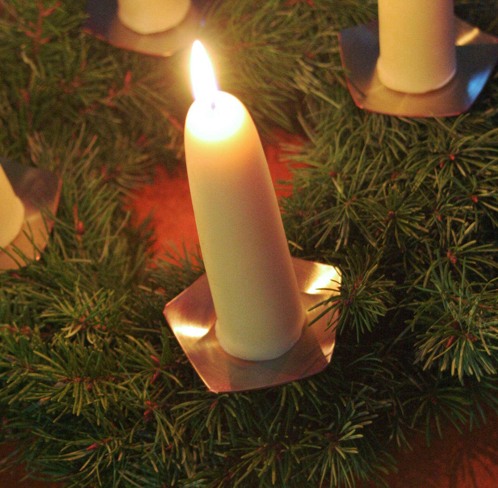 Adventskerze aus Bienenwachst mit einem Kupfer-Kerzenhalter auf einem Adventskranz