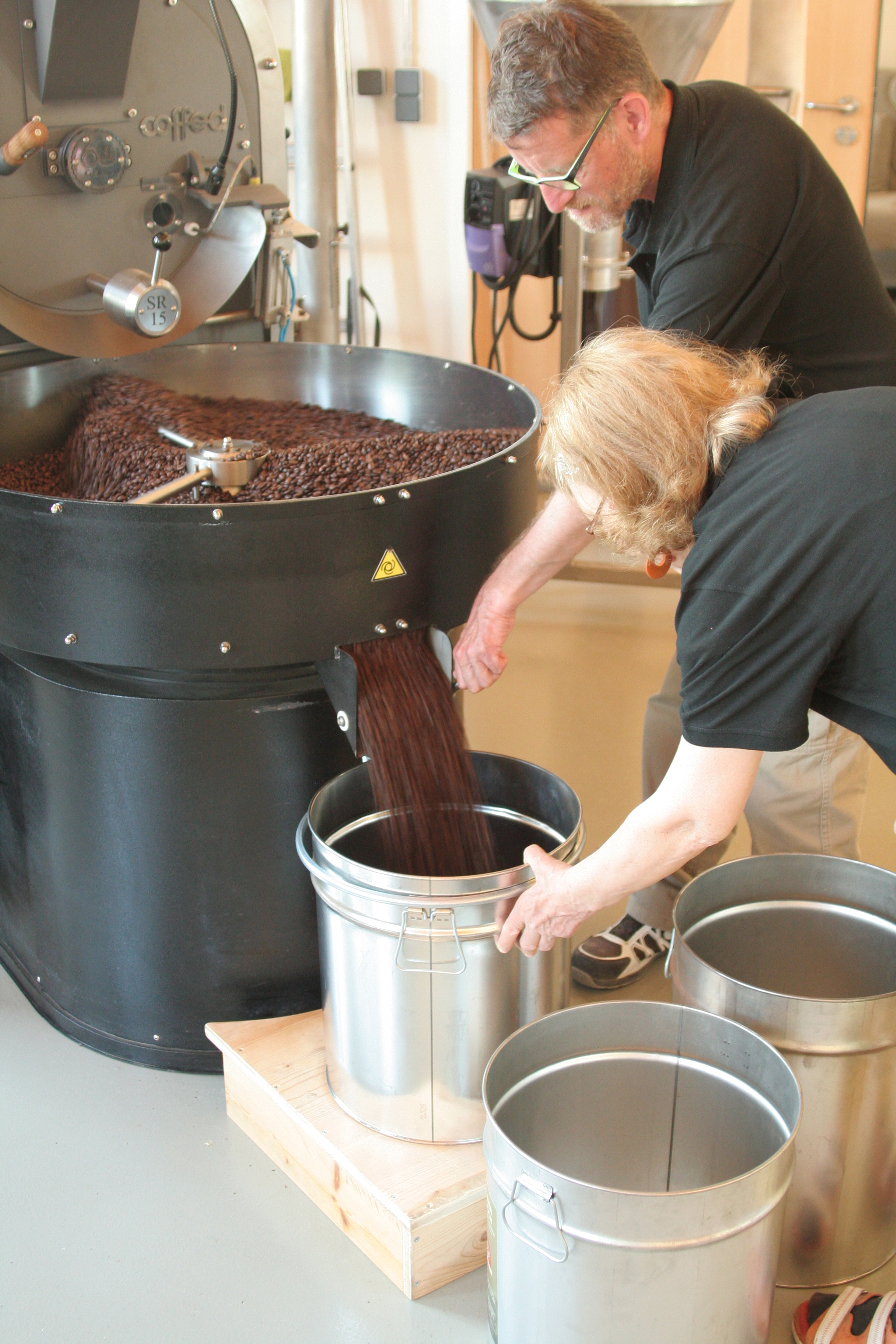 Zwei Mitarbeiter füllen die gerösteten Kaffeebohnen in einen Behälter